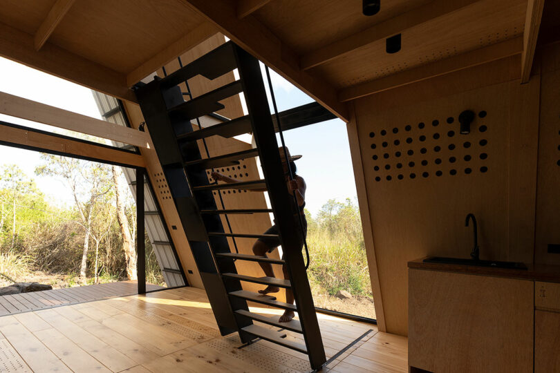 angled interior view of minimalist cabin with woman climbing the stair ladder