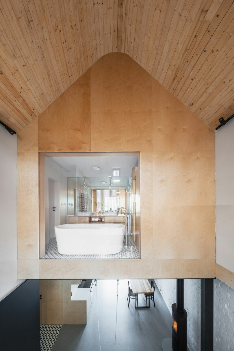 interior view looking at suspended wood room above living space below with window into bathroom with tub in front of window