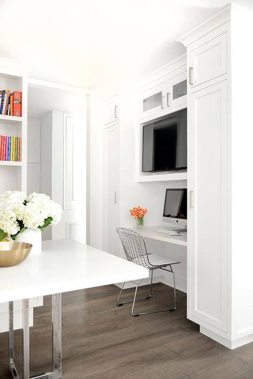 nook features a white floating desk paired with a Bertoia Chair tucked under a flat panel television sitting on a shelf flanked by floor to ceiling cabinets.