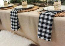 a cozy rustic winter table setting with plaid napkisn, woven placemats, evergreens, candles and antlers and jars with candles