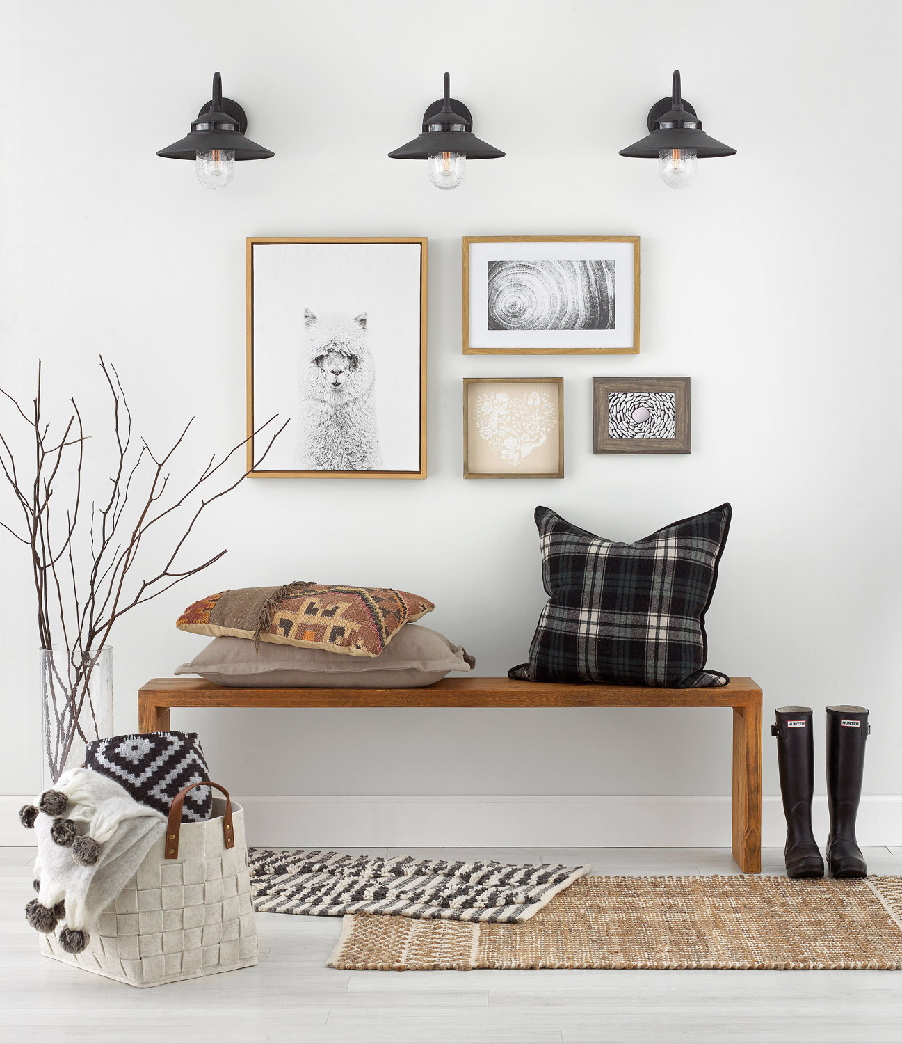 A bench with a pillow in an entryway with shoes beside it and framed pictures on the wall.