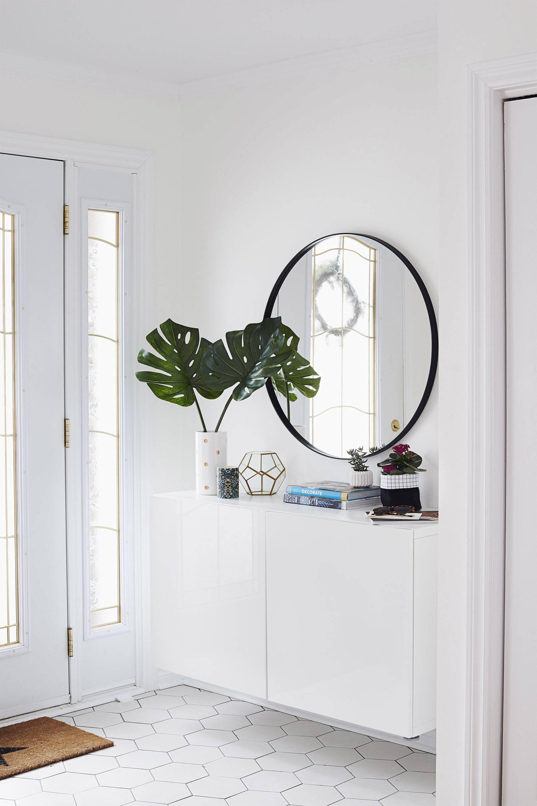 White entryway with storage and a large circular mirror.