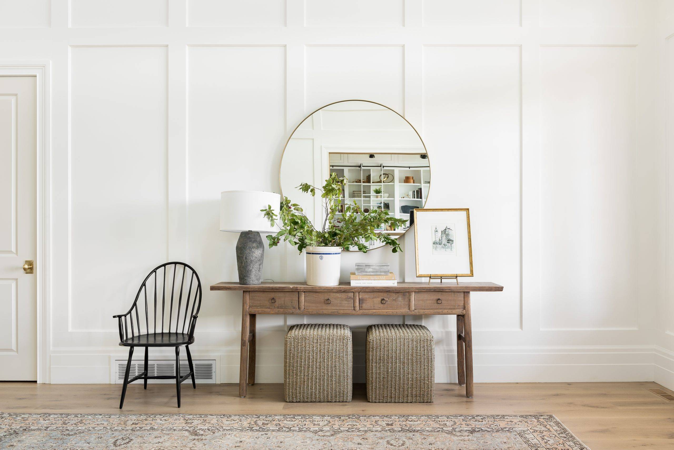 Entryway that hosts a wood chair and a table that's holding a plant, lamp, and framed picture.