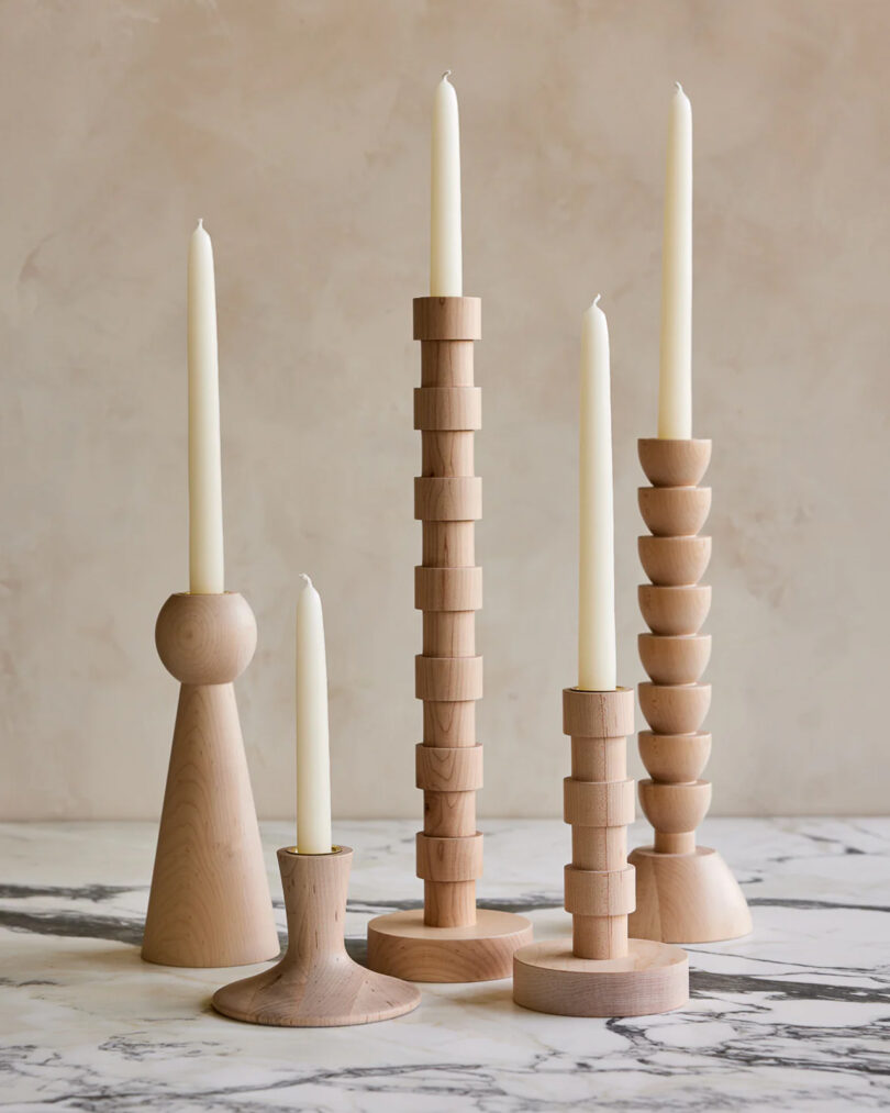 five light wood candle holders of different heights and shapes with white tapers