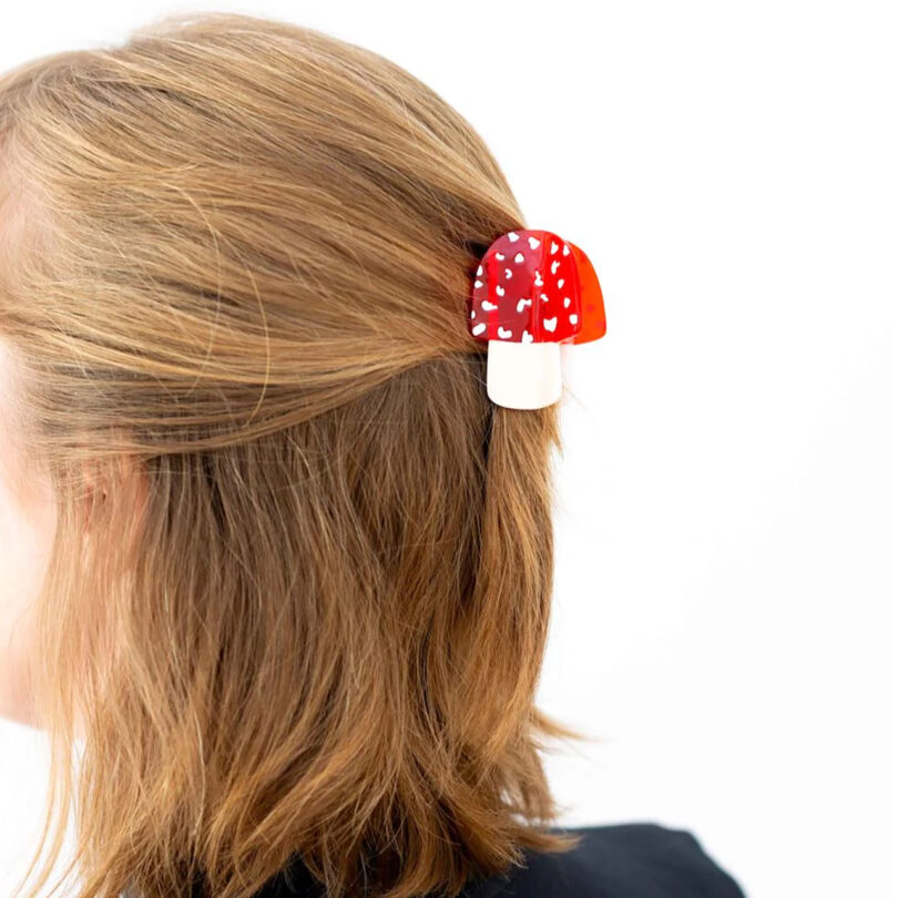 light-skinned person with light brown hair models a red and white mushroom hair clip