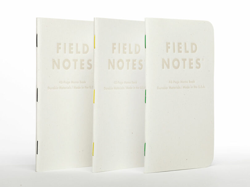 three thin white notebooks with colorful stitching standing up