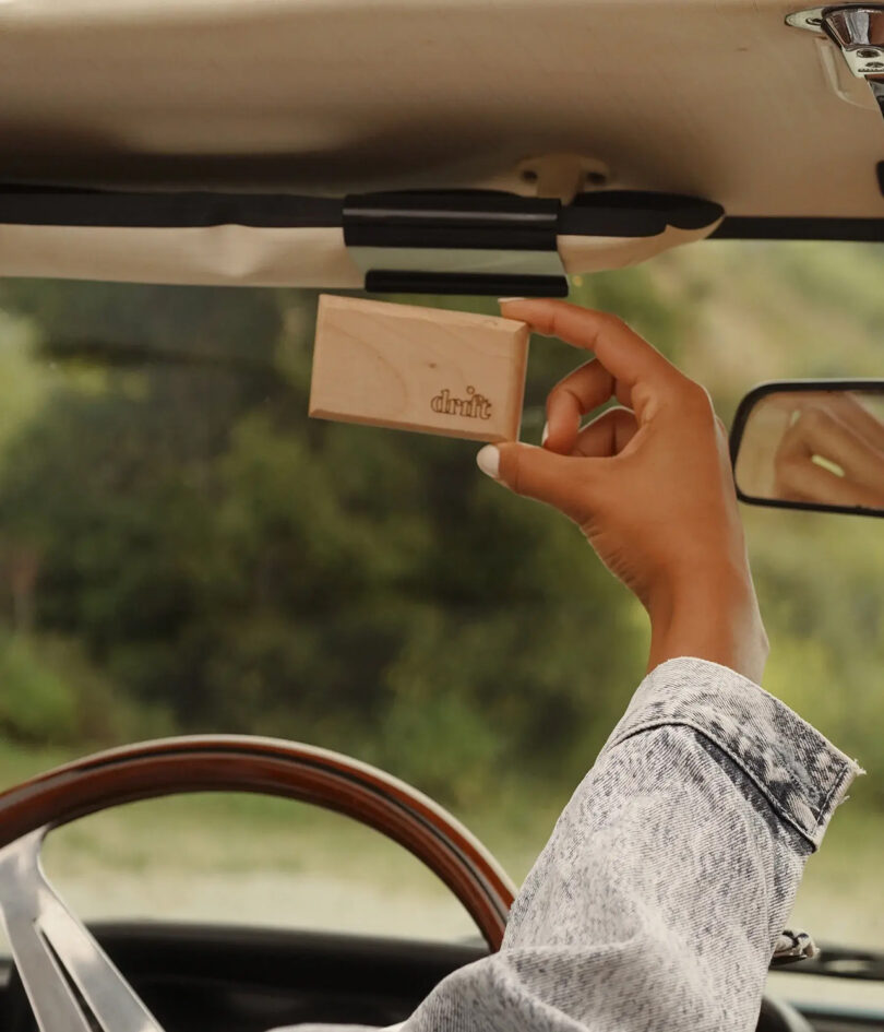 brown-skinned hand places a wood air freshener on a sun visor