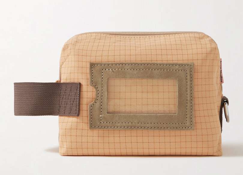 Tan and orange grid patterned toiletry bag with brown nylon pull handle on left and tag holder in center.