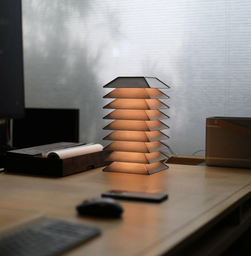 Multi-tier pagoda shaped desk lamp on desk, dimly illuminated.