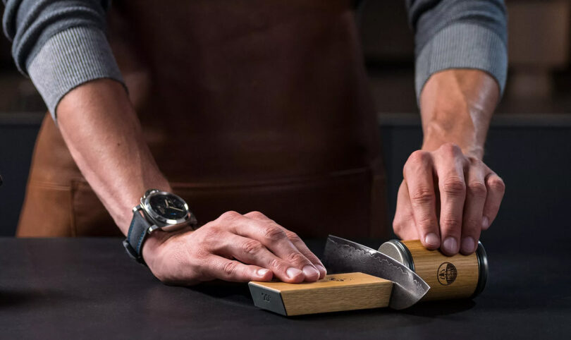 Person wearing long sleeves and a wristwatch sharpening a knife using HORL 2 magnetic sharpener
