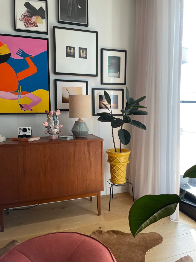 Living room setting with lots of wall art, with large ice cream cone shaped planter with rubber tree planted in it.