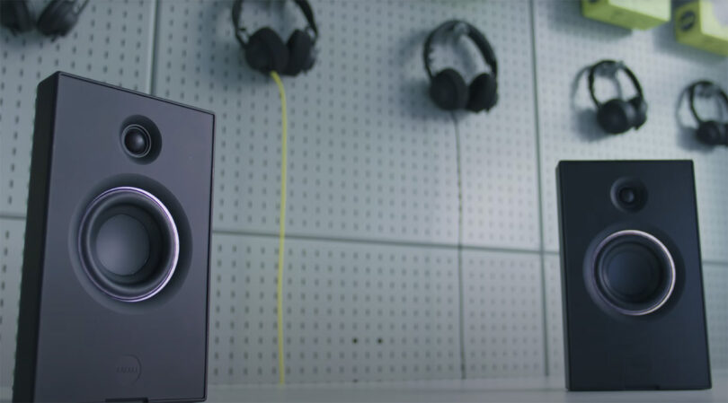 Aiaiai UNIT 4 studio monitor speaker pair on a table with a pegboard display behind it holding up headphones.