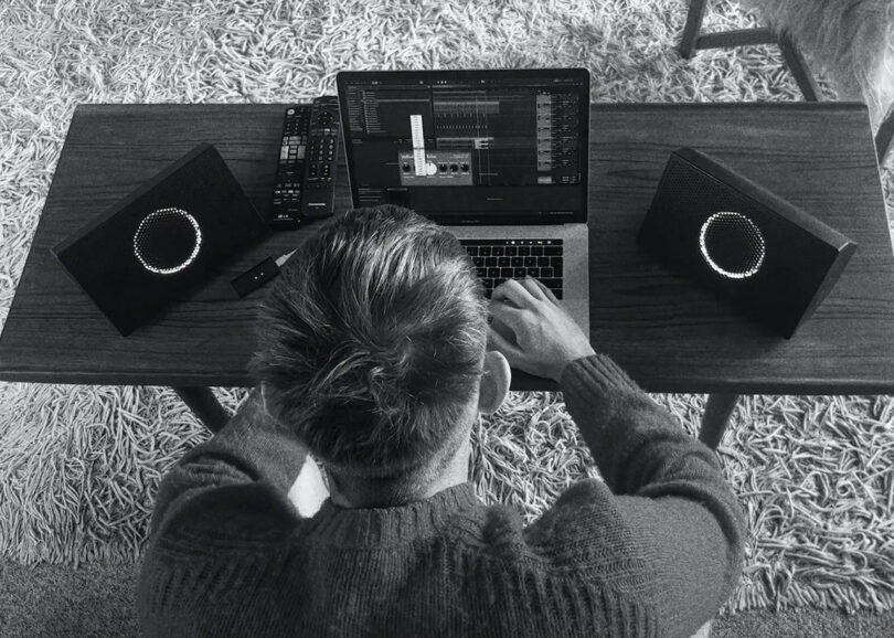 Black and white image of man at his laptop seen from overhead with two AIAIAI UNIT-4 studio monitors on each side of the computer.