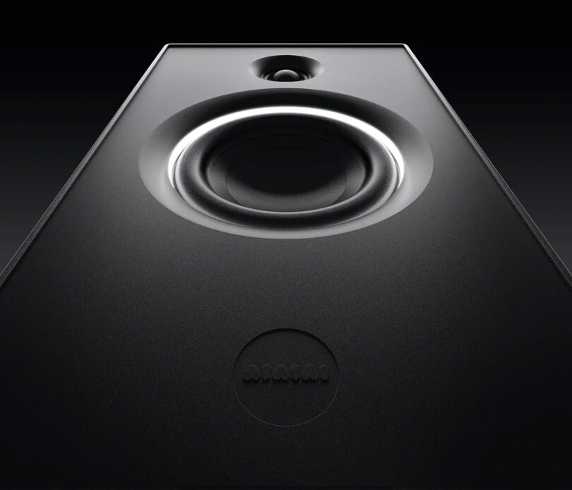 Distorted view of UNIT-4 studio monitors viewed from the bottom up, emphasizing the speaker's midrange and tweeters. A subtle AIAIAI logo is visible in the lower portion slightly shadowed.