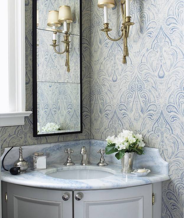 Gorgeous blue and gray bathroom with gray corner bow front bathroom vanity paired with blue stone countertop and black rectangular bathroom mirror, Blue and gray flocked wallpaper in bathroom and antique brass French sconces.