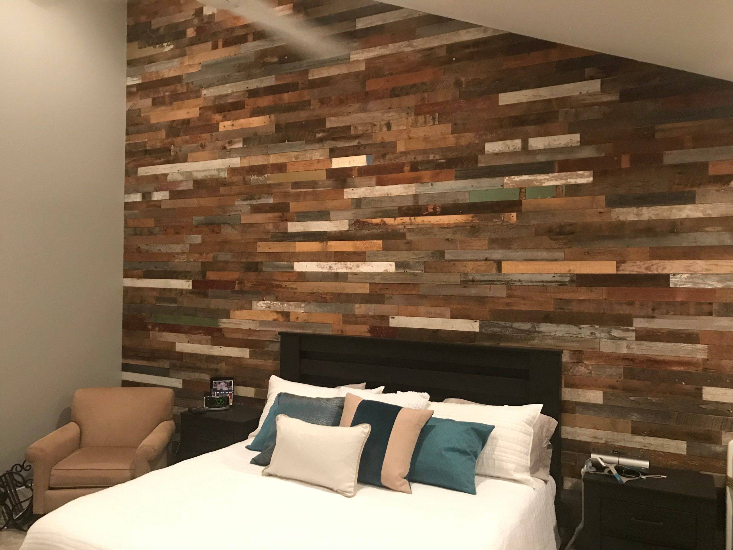 Barn plank wall in a bedroom with white bed and small single-seat chair.