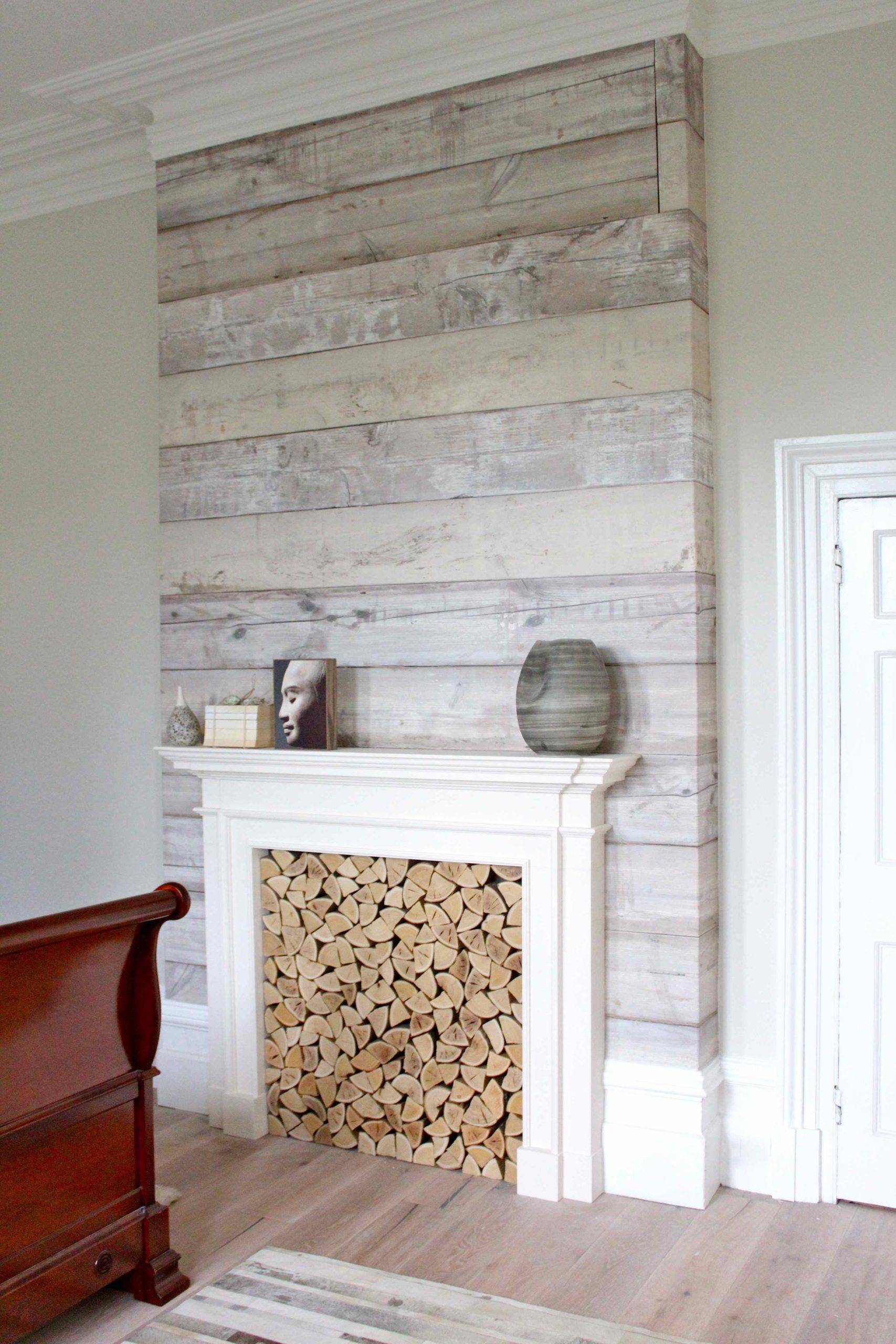 Whitewash wood accent wall with a fireplace filled with quarter logs.