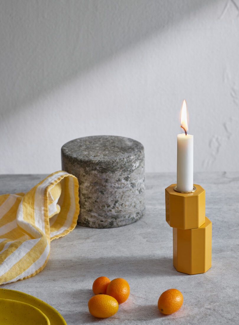 modern orange candle holder with an illuminated white candlestick on a styled surface