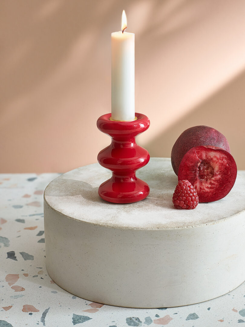 modern red candle holder with an illuminated white candlestick on a styled surface