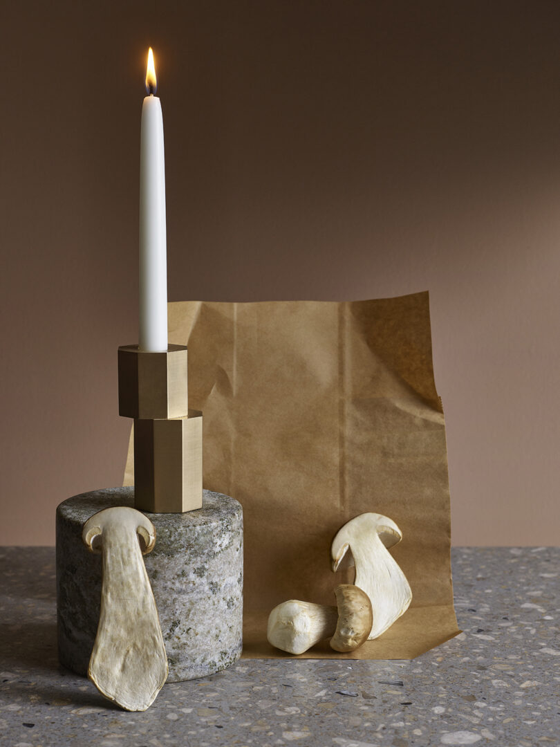 modern brass candle holder with an illuminated white candlestick on a styled surface