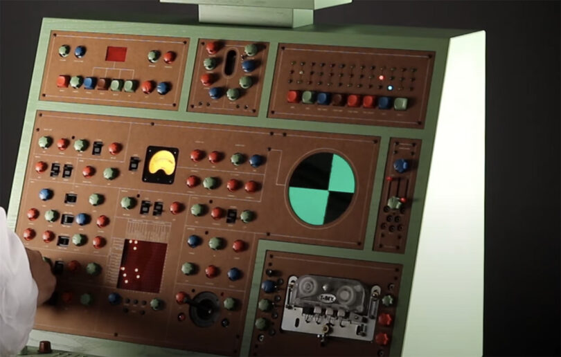 ATOM-IC green and brown wood cabinet synthesizer with small keyboard and layout of numerous colorful dials, switches, sliders and buttons controls. Oscillator display shows a green checkerboard pattern.