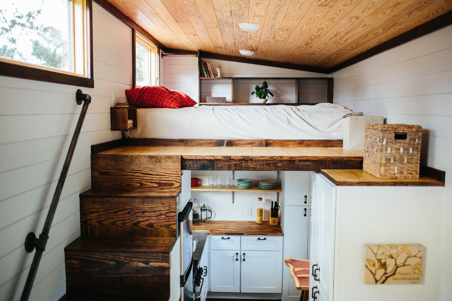 Interior of a tiny home that has wooden stairs leading to the bed while the kitchen is tucked underneath.