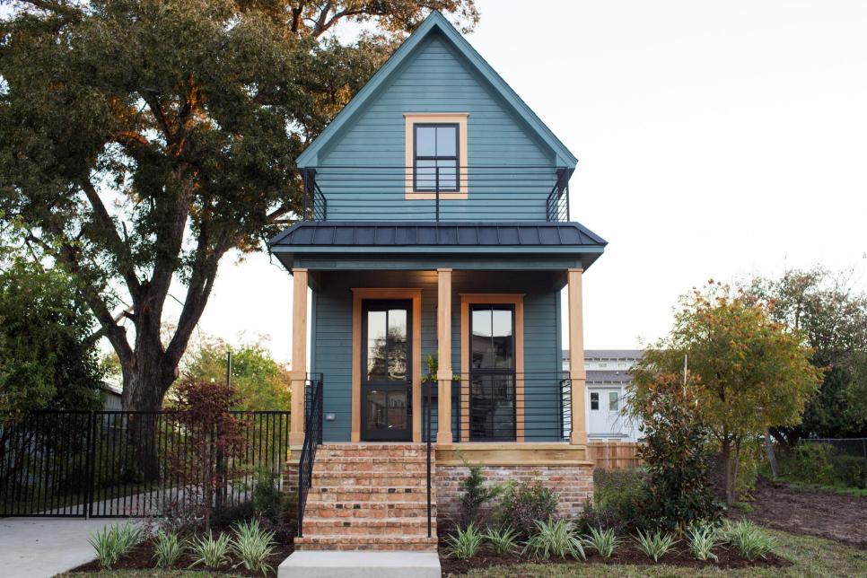 Blue exterior of a tiny home that has black fencing, brick stairs, and wood beams.