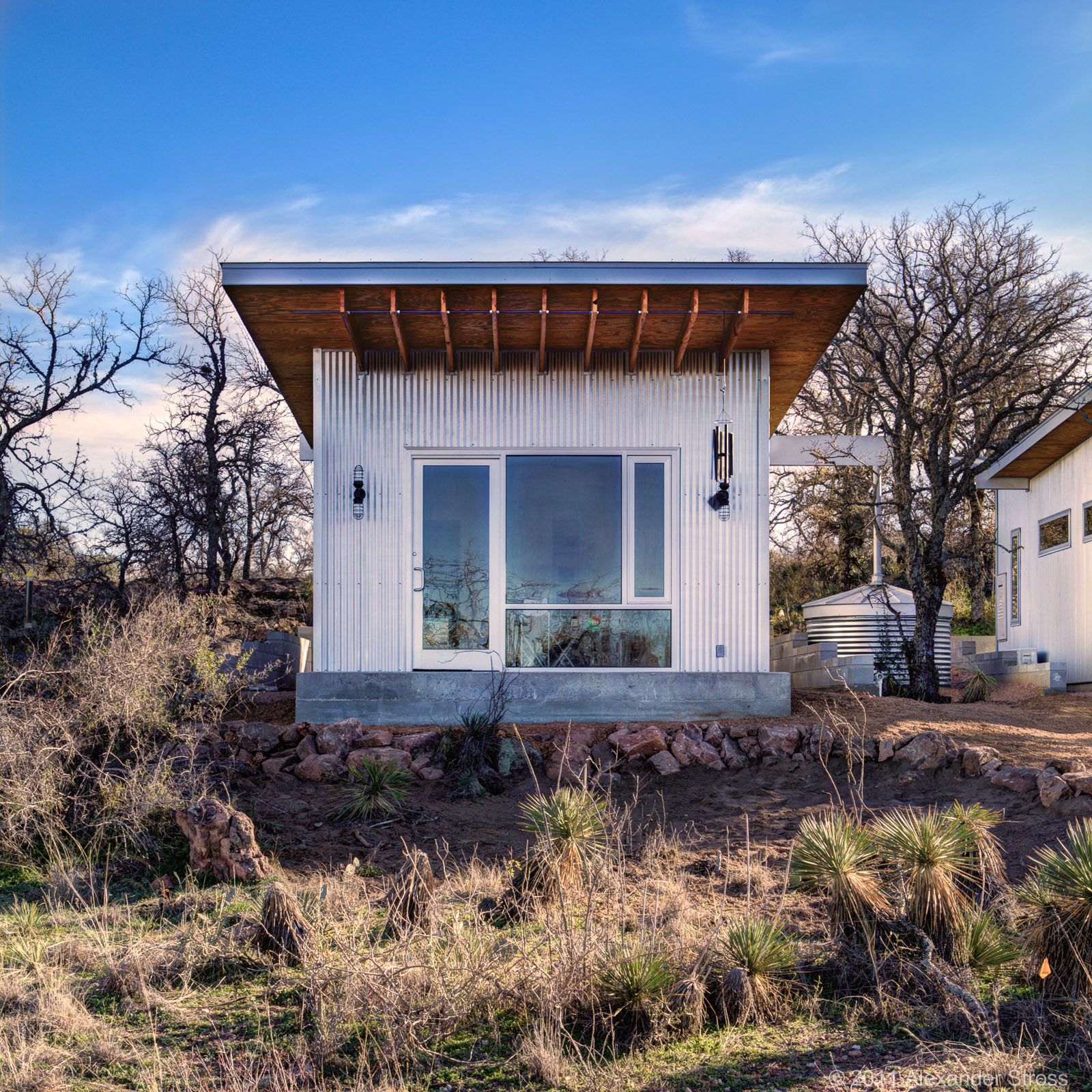 Tiny home with a sheet metal exterior that's in an area with trees and bushes.