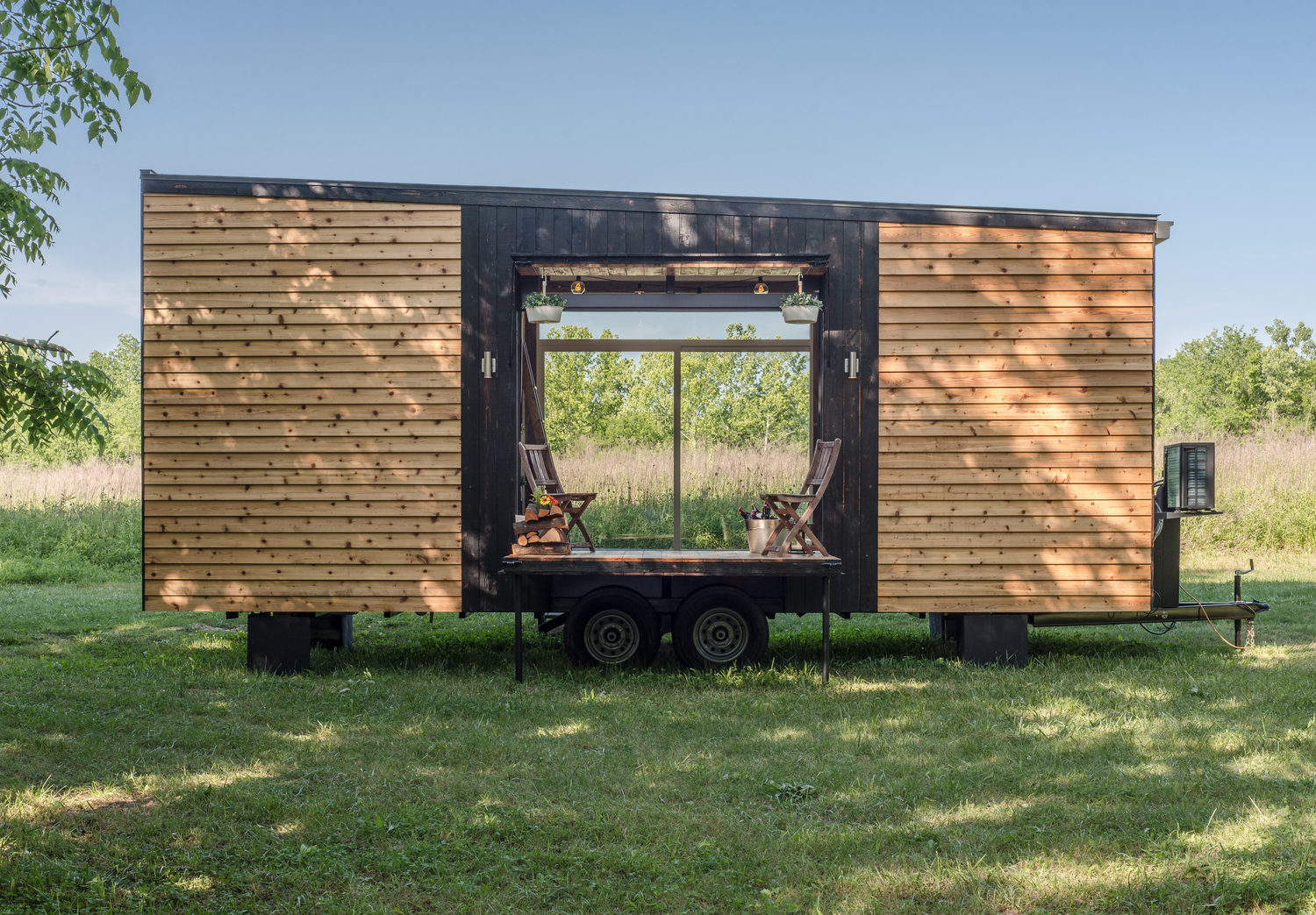 Tiny home on a trailer frame finished with wood on the exterior and two large windows.