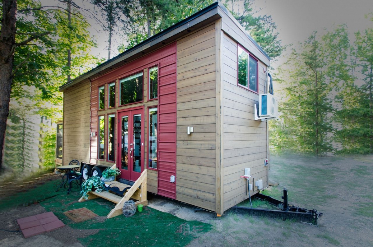 Tiny home on trailer frame, featuring wood exterior with red metal frames for windows.