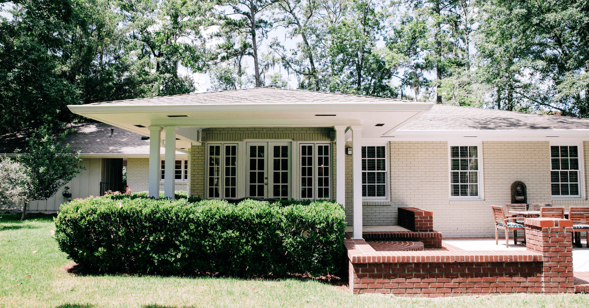 Older ranch style house with green bush upfront.