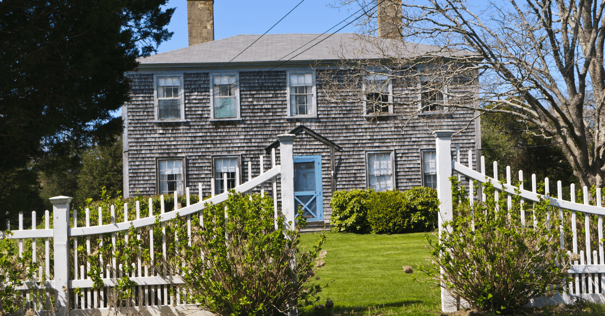 Older Cape Cod style house with double chimneys and a blue screen door.