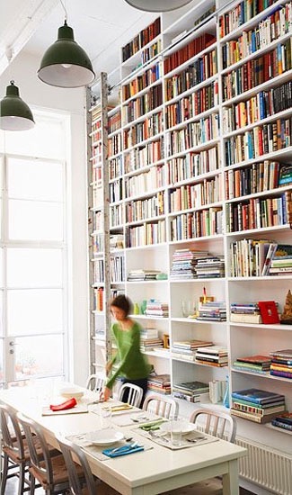 A woman, setting up a table in a room with large bookshelves.