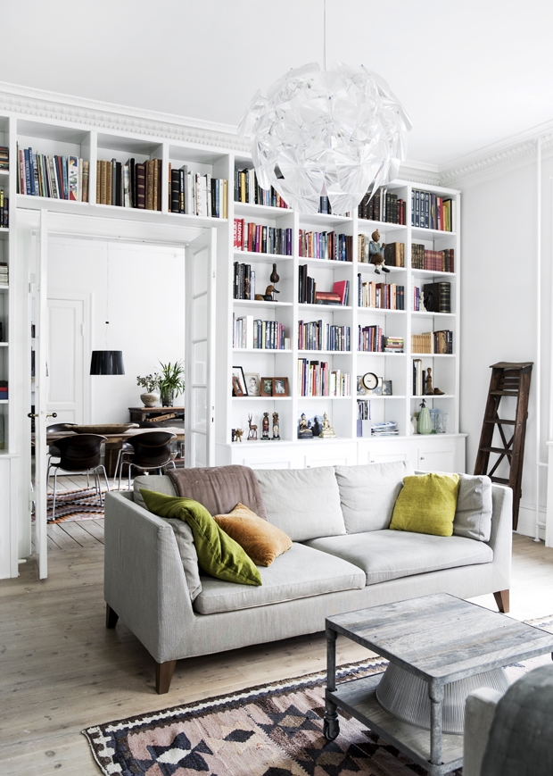 A cozy living space with white walls and bookshelves, featuring a grey couch with throw pillows.