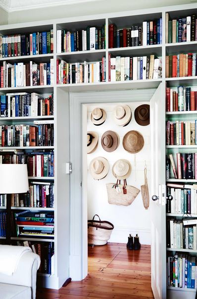 A room featuring a white couch and bookshelves flanked by another room with hats mounted on the wall.