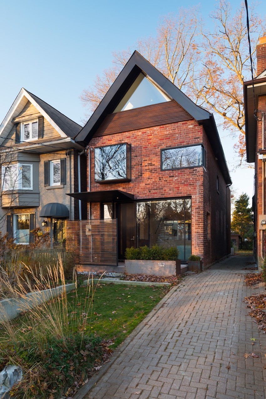 Driveway leading up to a red brick house with uniquely shaped windows.