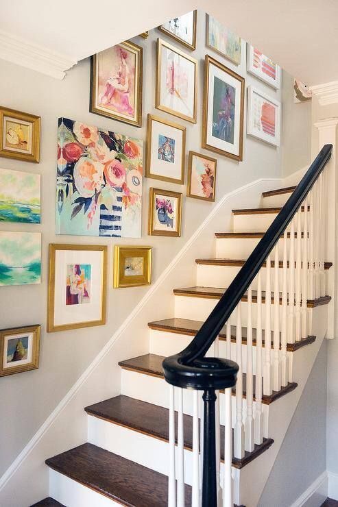 A bright stairway with a picture gallery of various sizes framed in gold frames.