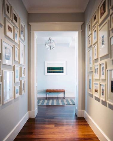 Hallway gallery with framed pictures on both walls, while a leather bench is at the end of the hall.