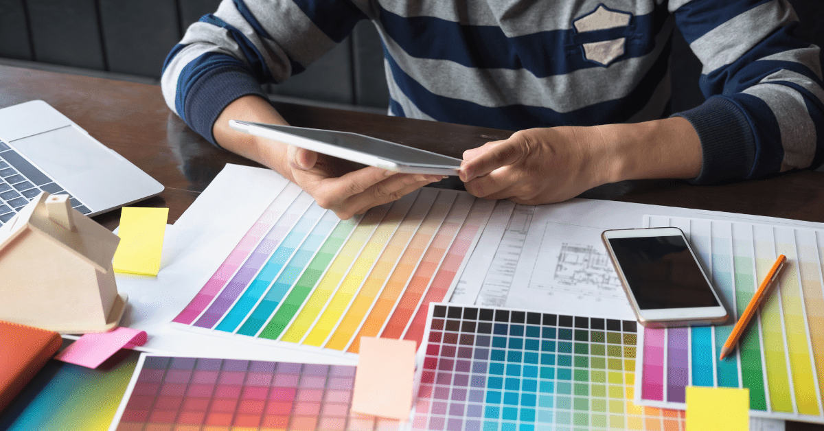 Person holding a tablet while the table has sheets of color options.