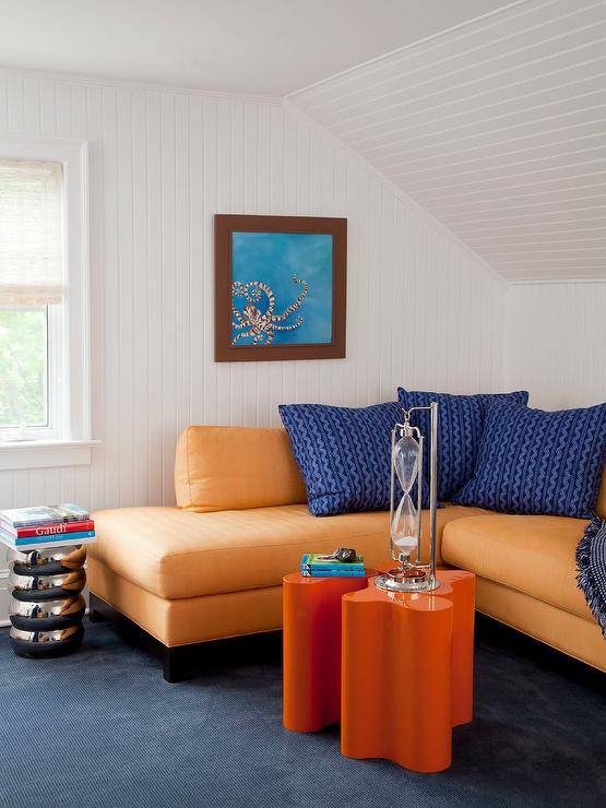 Modern attic orange and blue family room with beadboard trim features an orange sectional with blue pillows, orange lacquer cluster accent tables, atop blue carpet.