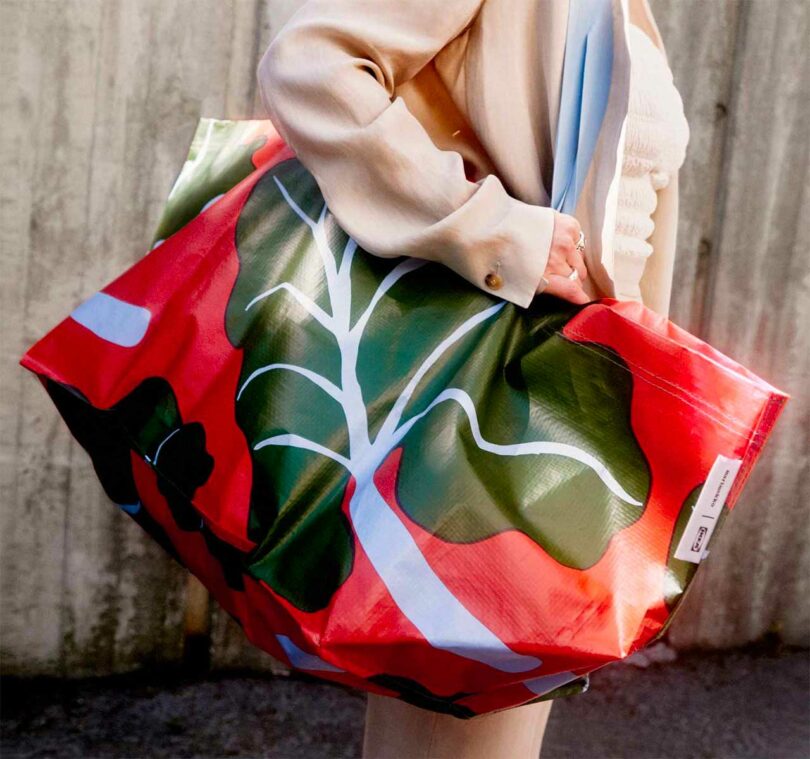shot of a person's mid-body turned sideways holding a large overized red tote with a large green leaf on it