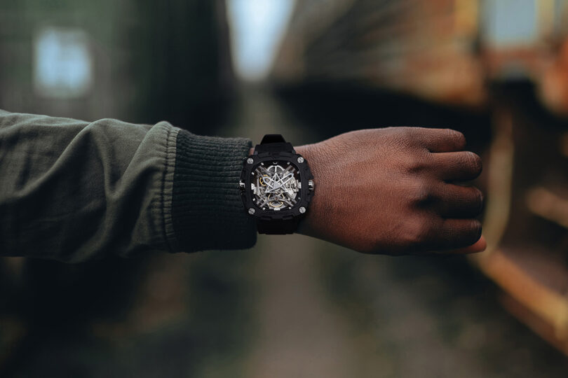 Arm in green jacket wearing the Eye of Horus wristwatch with blurred outdoor background