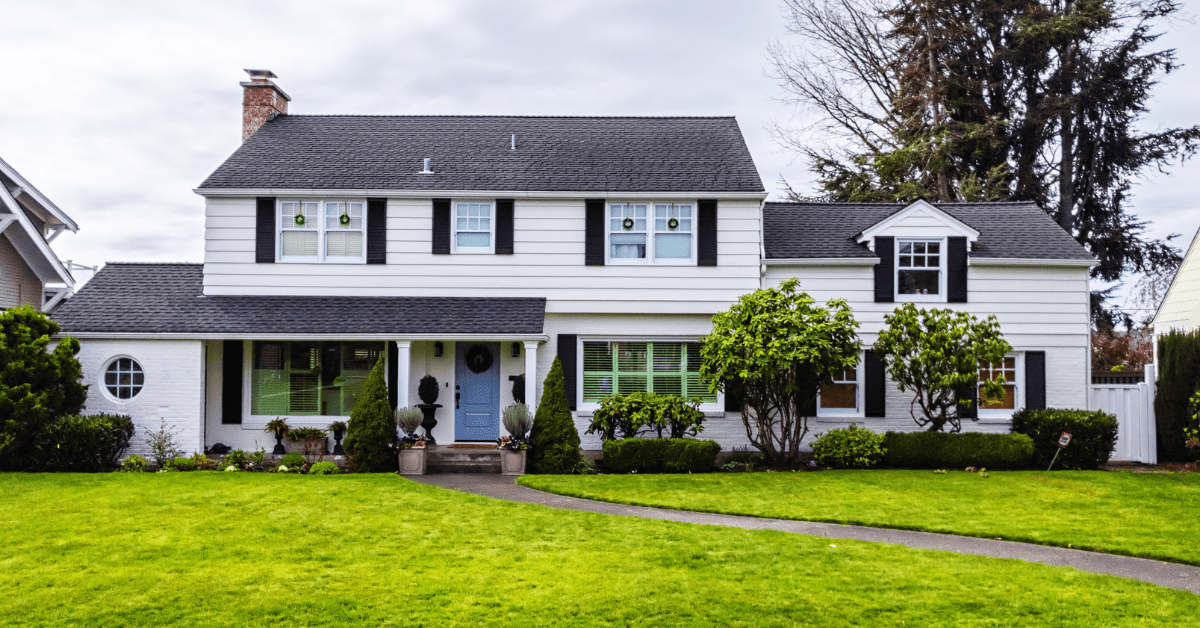 Exterior of a white colonial styled house with well kept grass and curvy walkway.