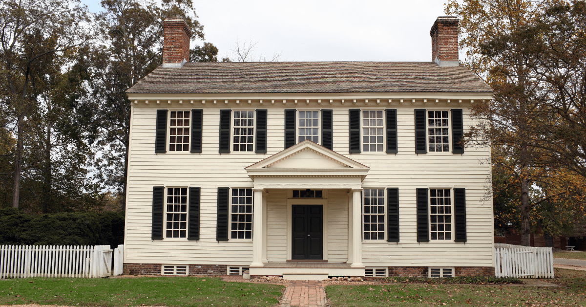 An exterior of a white colonial-styled house, featuring two chimneys and symmetrical styling.