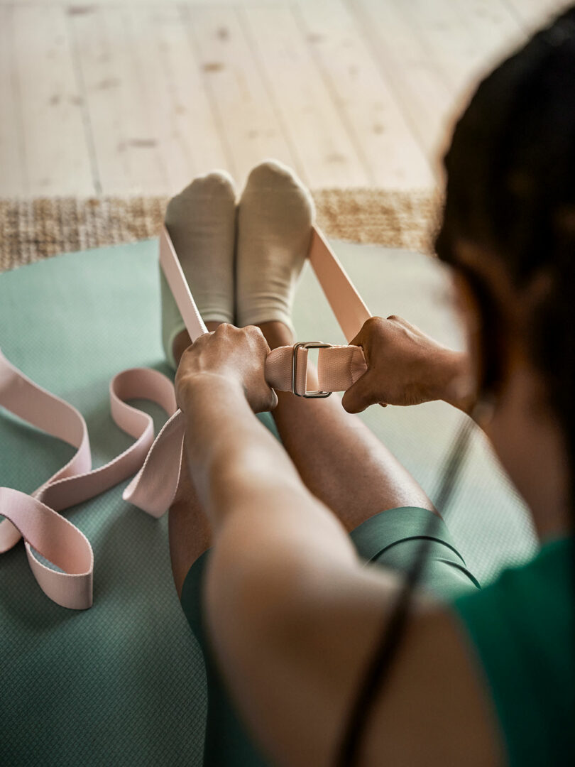 view from behind woman leaning forward on floor with pink band wrapped around feet stretching