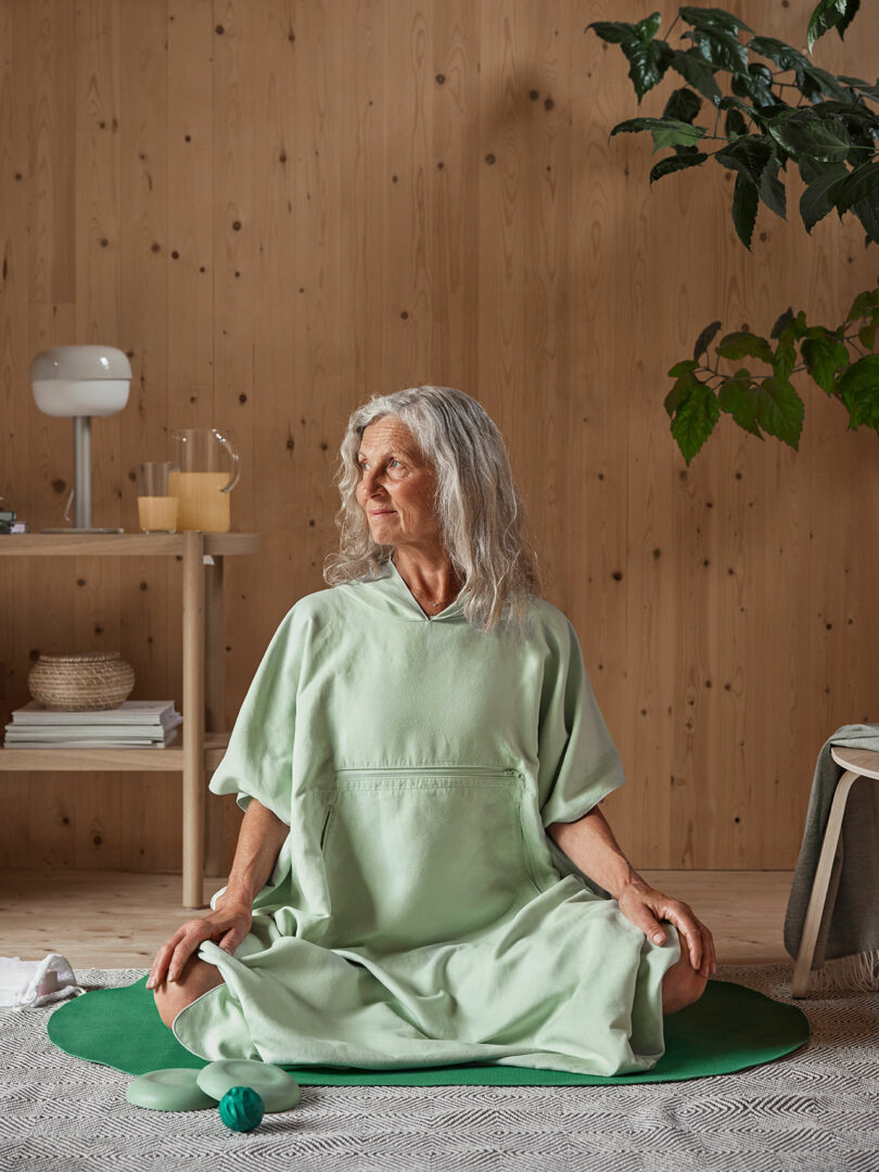 older woman with gray hair in light green casual sweatsuit sitting on dark green fitness mat