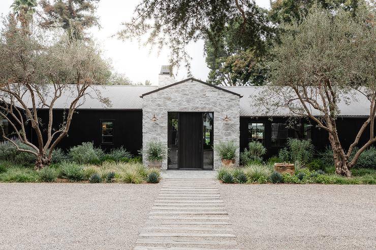 Modern one story farmohouse boasts a gray stone exterior and a plank front door flanked by sidelights.