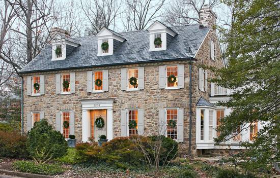 Cottage home with stone and stucco exterior accented with sash windows with pale gray shutters and a slate tiled roof framing dormer windows.