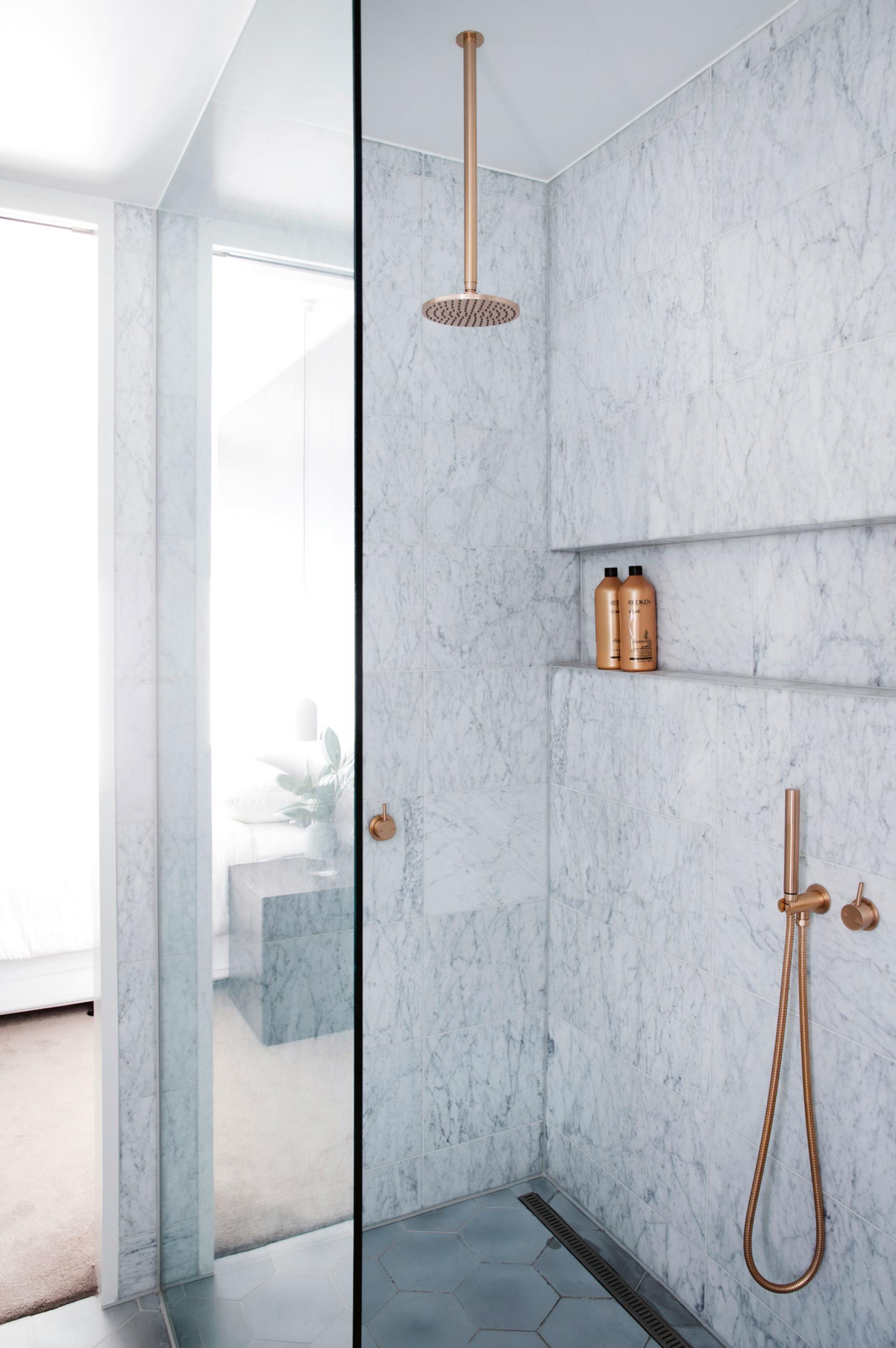 A luxurious bathroom featuring elegant marble walls and a sleek shower finished with touches of copper.