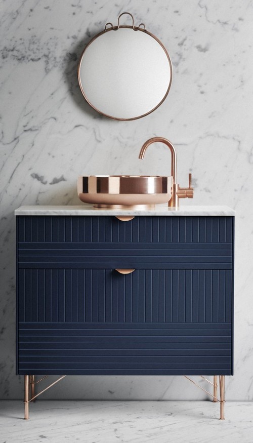 Bathroom with marble walls, blue vanity, and copper sink and fixtures.